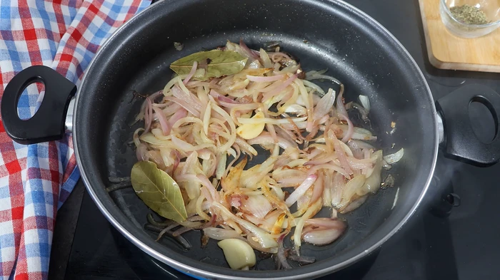 Cazuela con cebolla morada, blanca, ajo y laurel pochándose