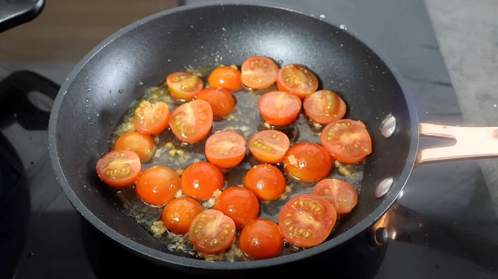 Sartén con tomates cherry cortados y cocinados en ajo y aceite