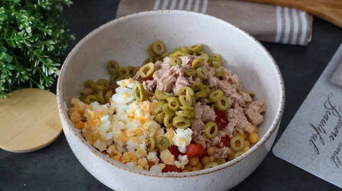 Ingredientes listos para ensalada de garbanzos en bol: atún, huevo, aceitunas, tomate