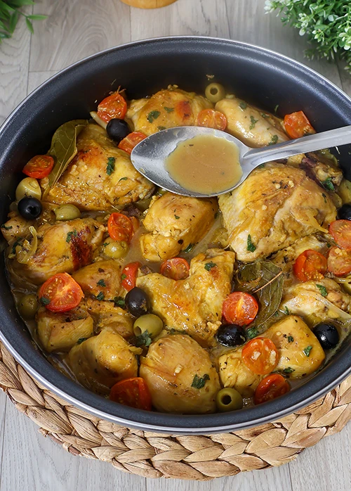 Cuchara sirviendo salsa de guiso de pollo mediterráneo con cherry y aceitunas