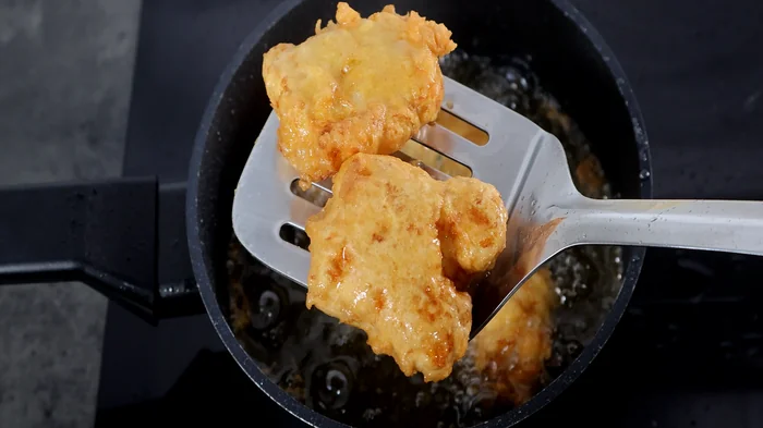 Piezas de kibbeling doradas recién fritas sobre espumadera.