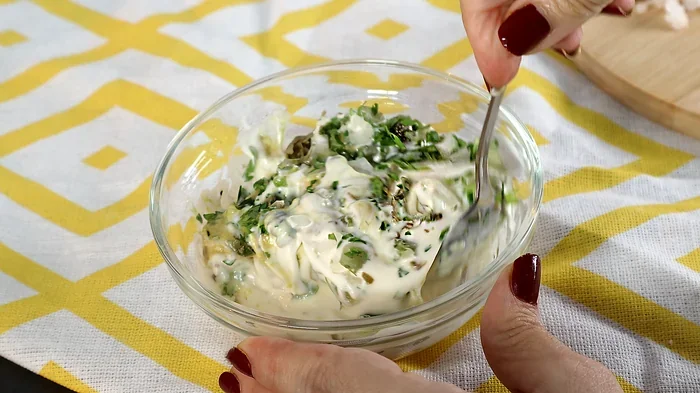 Mezclando salsa remoulade casera con mayonesa, mostaza, pepinillos, alcaparras y hierbas para acompañar el kibbeling.