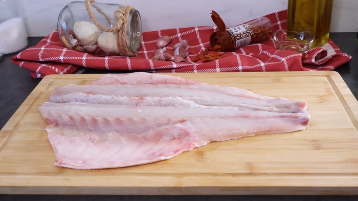 Lubina fresca abierta a la espalda sobre tabla de cocina, lista para la receta.