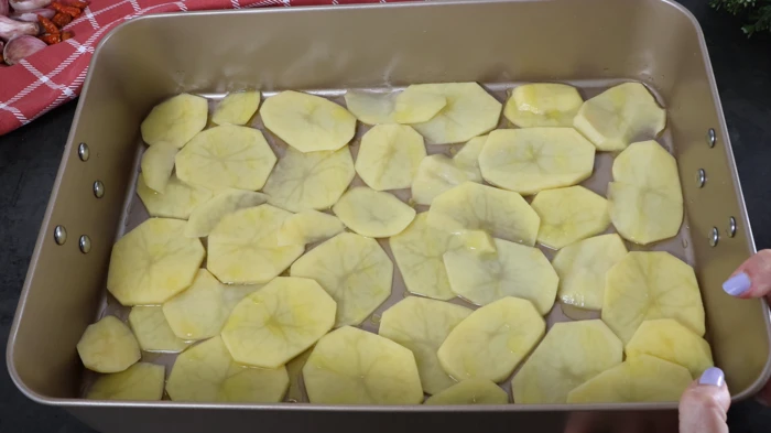 Patatas cortadas en rodajas con aceite de oliva en bandeja de horno.