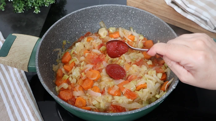 Añadiendo concentrado de tomate al sofrito para la ternera guisada con champiñones.