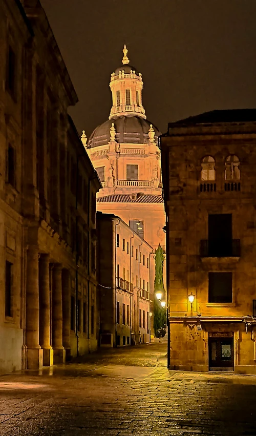 Cúpula iluminada de la Clerecía de Salamanca vista desde una calle empedrada