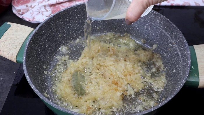 sofrito de cebolla con hoja de laurel mientras se añade vino blanco