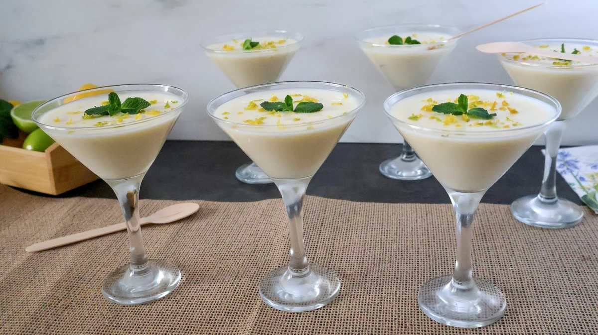 Lemon posset clásico servido en copas, postre británico de limón decorado con ralladura y menta
