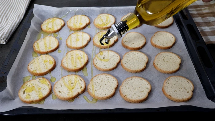 Rebanadas de pan en bandeja de horno rociadas con aceite de oliva