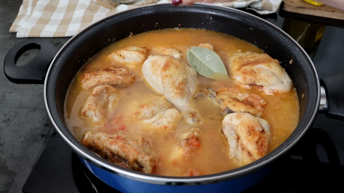 Añadiendo caldo de ave y laurel al guiso de pollo en salsa