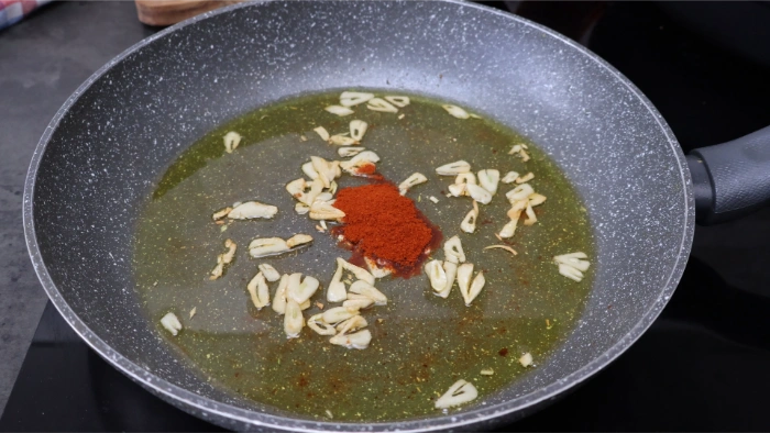 Sartén con ajos fileteados dorados en aceite y pimentón de la Vera recién incorporado con el fuego apagado, base de la ajada del bacalao a la tranca