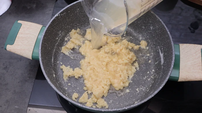 Añadiendo el caldo de cocción de las gambas al roux de mantequilla y harina para hacer la bechamel del relleno de rissóis portugueses