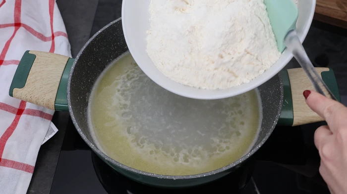 Añadiendo toda la harina de golpe al agua con mantequilla hirviendo para hacer la masa escaldada de rissóis portugueses