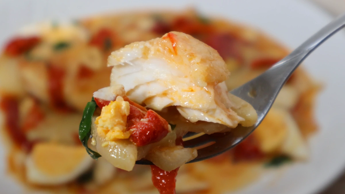 Porción de bacalao a la tranca servida en tenedor con patatas y pimientos