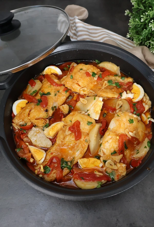 Cazuela vista lateral con bacalao a la tranca zamorano completo: lomos en ajada roja con pimientos asados, patatas guisadas, huevo duro y perejil fresco