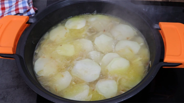 Rodajas de patata cociendo en caldo de pescado con cebolla en cazuela, acompañamiento del bacalao a la tranca zamorano