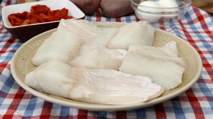 Lomos de bacalao desalado en un plato, con pimientos asados, patatas y huevos como ingredientes principales del bacalao a la tranca