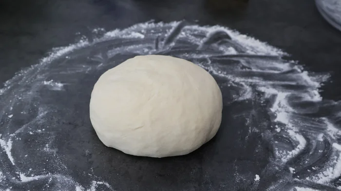 Bola de masa de pizza lista para levar sobre superficie enharinada