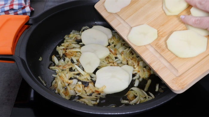 Rodajas de patata añadiéndose a la cazuela con cebolla pochada, antes de agregar el caldo de pescado