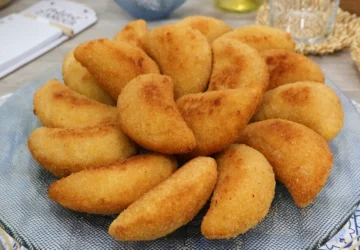 Bandeja de rissóis portugueses de gambas recién fritos, dorados y crujientes, servidos sobre mantel con motivo de azulejos portugueses