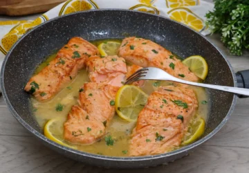 Salmón en salsa de limón jugoso servido en sartén con rodajas de limón y perejil fresco