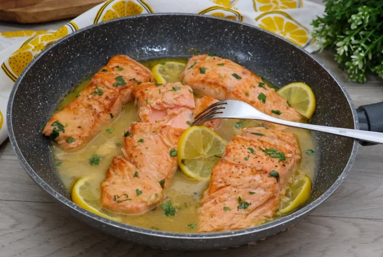 Salmón en salsa de limón jugoso servido en sartén con rodajas de limón y perejil fresco