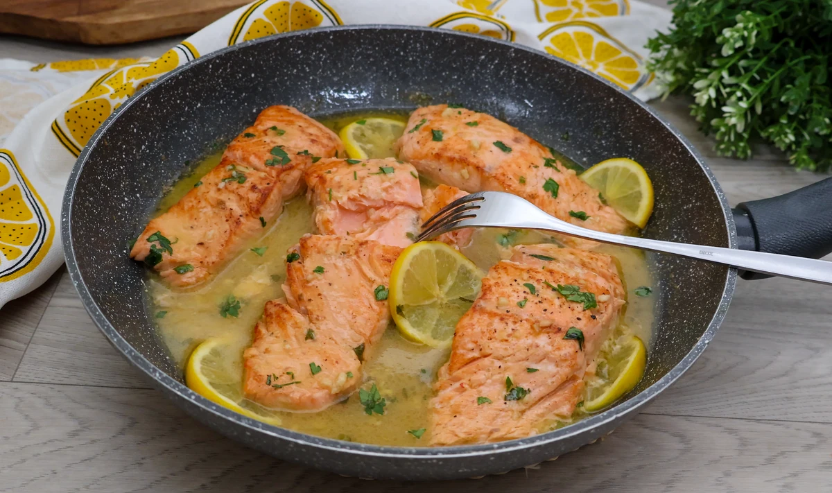 Salmón en salsa de limón jugoso servido en sartén con rodajas de limón y perejil fresco