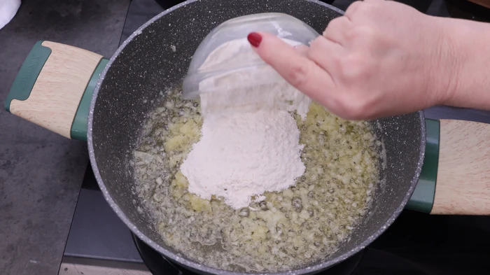Añadiendo harina al sofrito de cebolla pochada con mantequilla para preparar el roux base de la bechamel del relleno de rissóis portugueses