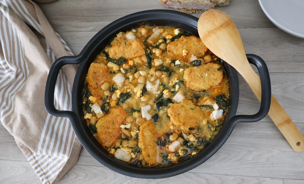 Potaje de vigilia con garbanzos espinacas bacalao y rellenos crujientes en cazuela vista cenital con cuchara de madera