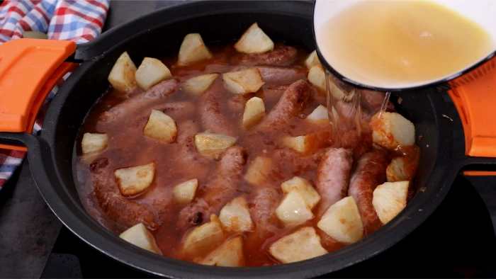 Vertiendo caldo de pollo sobre las salchichas y las patatas en la cazuela para terminar la cocción del guiso