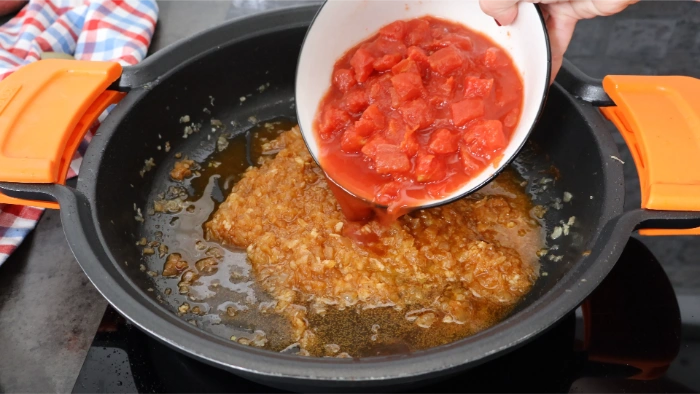 Incorporando tomate troceado en conserva al sofrito de cebolla y ajo con pimentón en cazuela