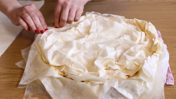 Manos cerrando y recogiendo las capas superiores de masa filo sobre el relleno de la kotopita