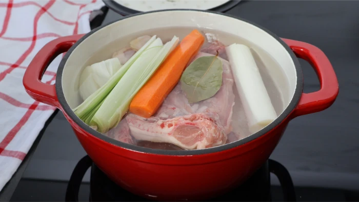 Traseros de pollo en cazuela con puerro, zanahoria, cebolla y laurel cubiertos de agua fría para preparar el relleno de la kotopita