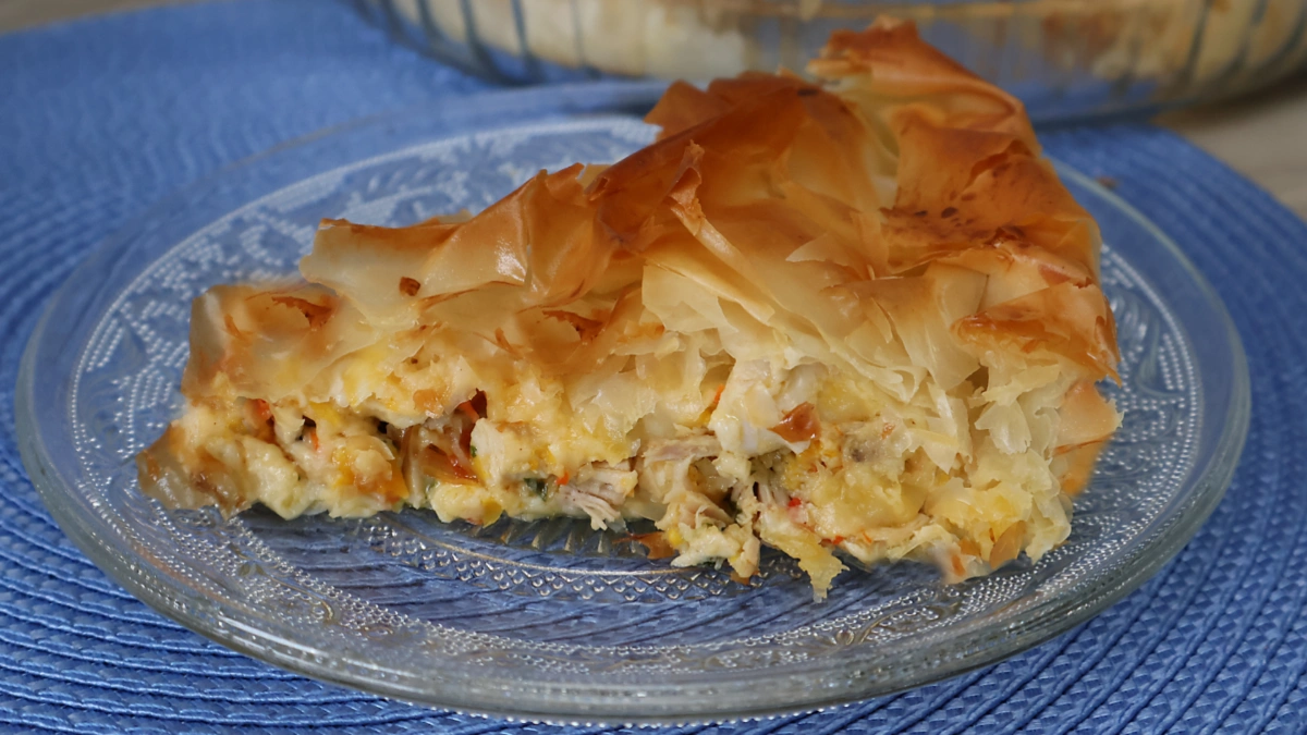 Porción de kotopita griega en plato con el relleno de pollo, queso y verduras visible entre capas de masa filo crujiente