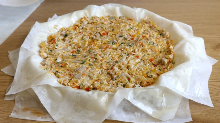 Relleno de pollo repartido sobre las capas de masa filo en fuente redonda antes de cerrar la kotopita