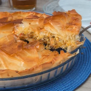 Pastel de pollo griego kotopita con masa filo crujiente y porción levantada mostrando el relleno de pollo, queso y verduras