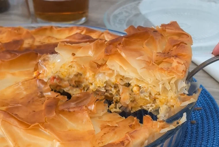 Pastel de pollo griego kotopita con masa filo crujiente y porción levantada mostrando el relleno de pollo, queso y verduras
