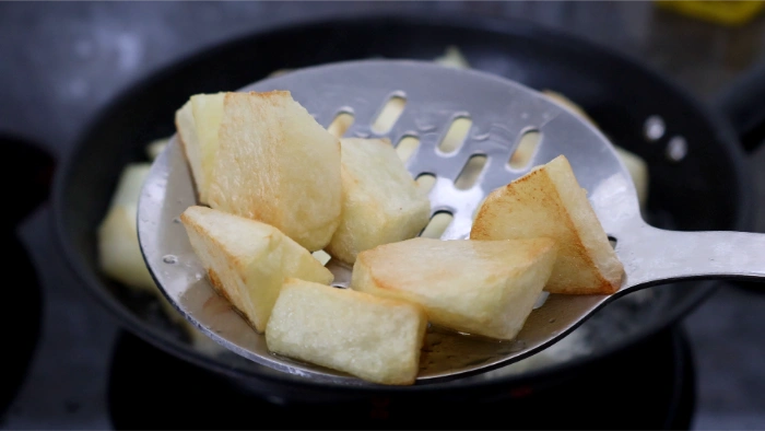Patatas en dados marcadas y doradas por fuera sobre espumadera, listas para añadir al guiso de salchichas