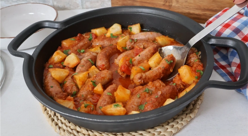 Cazuela de salchichas en salsa con patatas, tomate y perejil fresco, guiso terminado listo para servir
