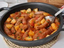 Cazuela de salchichas en salsa con patatas, tomate y perejil fresco, guiso terminado listo para servir