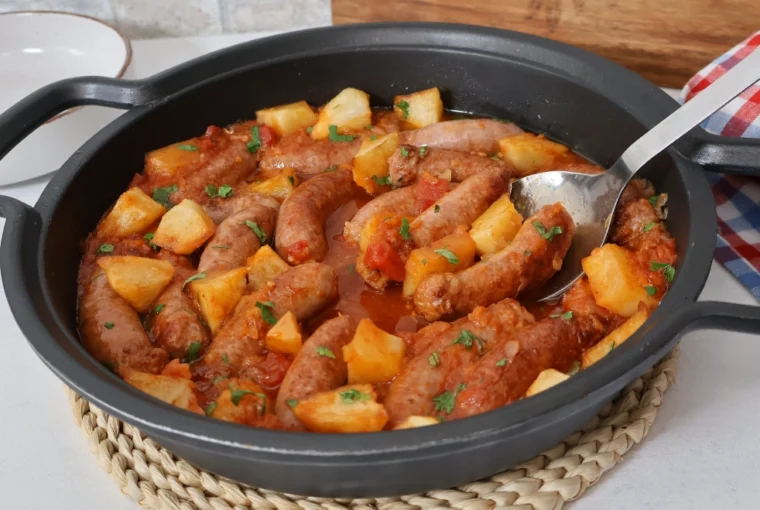 Cazuela de salchichas en salsa con patatas, tomate y perejil fresco, guiso terminado listo para servir