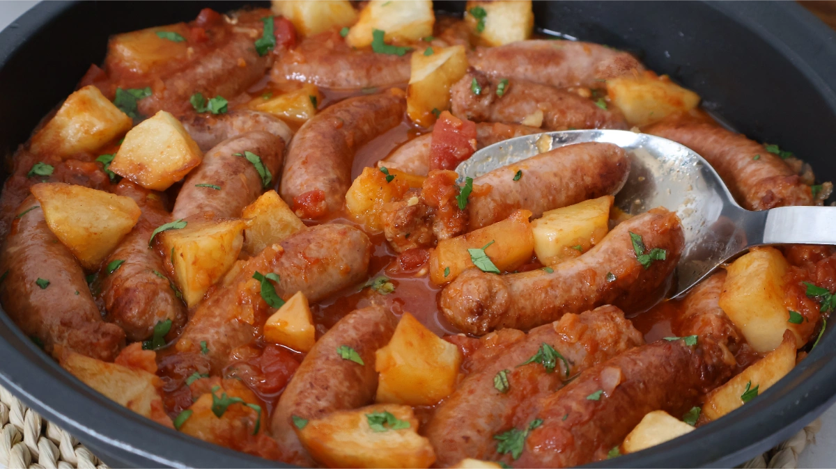 Cazuela de salchichas en salsa con patatas y trozos de tomate natural, receta fácil y económica para menús de diario