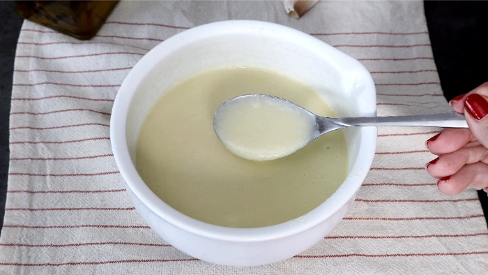 Cuchara mostrando la textura del aliño terminado del cojondongo extremeño — consistencia cremosa y fluida a base de pan, ajo y aceite de oliva