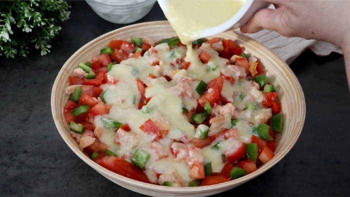 Aliño cremoso de pan, ajo y aceite de oliva vertiéndose sobre tomate y pimiento picados en bol de madera para preparar el cojondongo extremeño