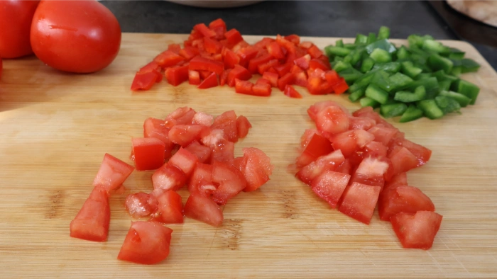 Tabla de madera con tomate maduro, pimiento rojo y pimiento verde cortados en dados para el cojondongo extremeño, las hortalizas siempre picadas nunca trituradas