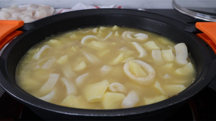 Añadir caldo de pescado al guiso de patatas con merluza y calamares