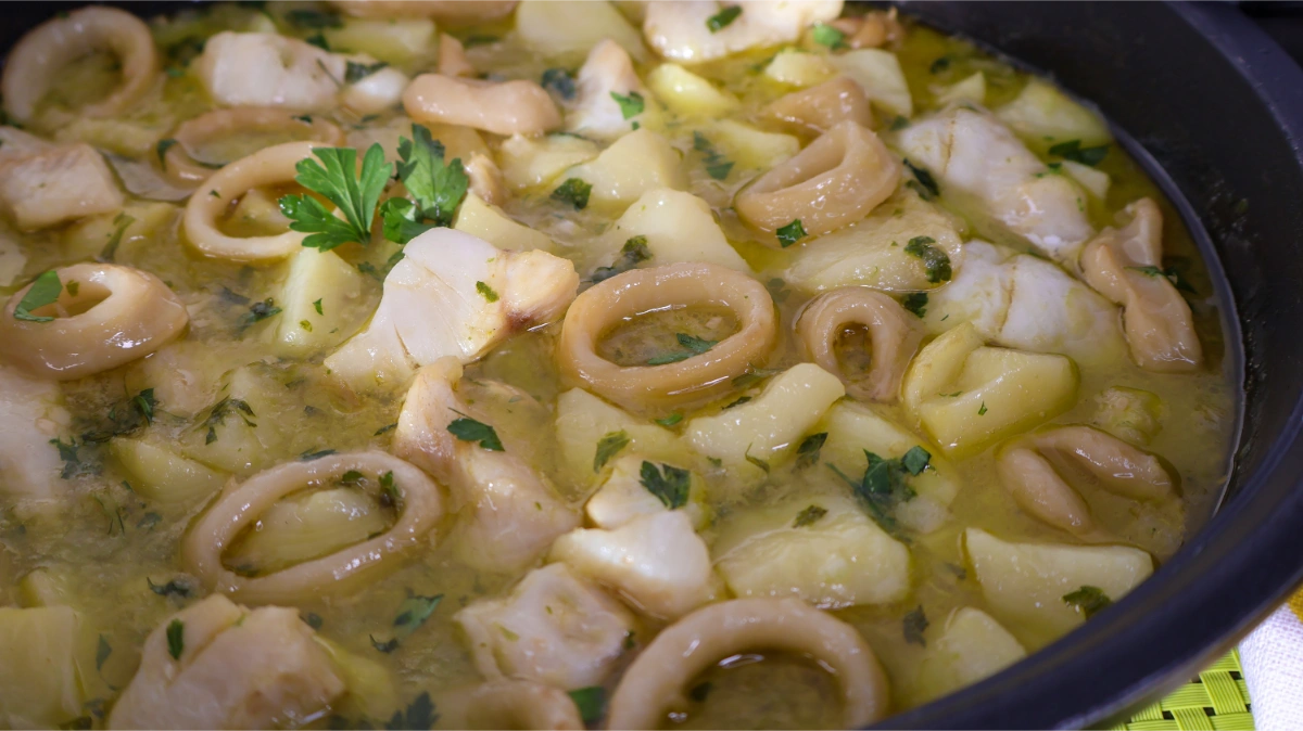 Detalle de la cazuela con merluza, calamares y patatas en salsa verde brillante