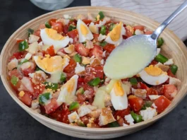 Cuchara vertiendo aliño cremoso de pan y ajo sobre cojondongo extremeño terminado con tomate, pimiento y huevo cocido en cuartos, listo para servir
