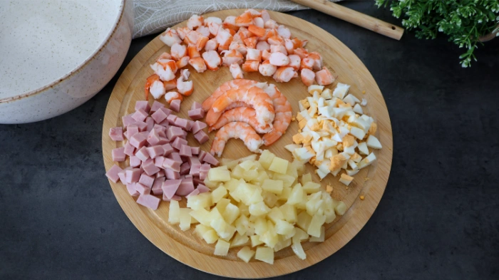 Langostinos, jamón de york, piña, huevo cocido troceados en una tabla para la ensalada de arroz