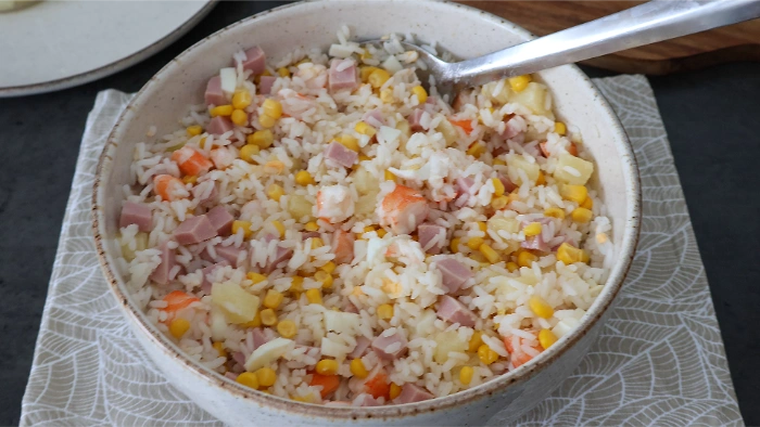 Ensalada de arroz con jamón, maíz, langostinos y piña mezclada en un bol